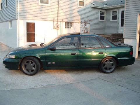 1998 Ford Taurus - A green sedan is parked in front of a house. The car has a sunroof and distinctive star-shaped wheels.