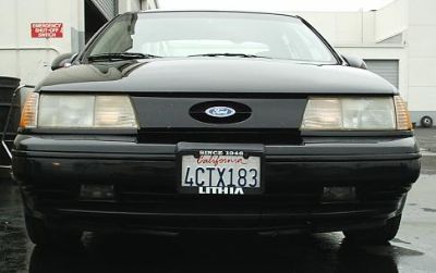 1998 Ford Taurus - A black Ford Taurus is parked outside a building, showing its front grille and headlights.