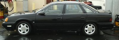 1998 Ford Taurus - Side profile of a black sedan with a spoiler, parked on a wet surface.