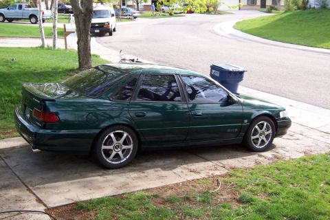 1998 Ford Taurus - Dark green 1998 Ford Taurus sedan parked on a driveway with a trash can nearby.