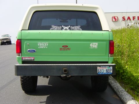 1990 Ford Bronco - Rear view of a green 1990 Ford Bronco with a white camper shell and various stickers on the tailgate.