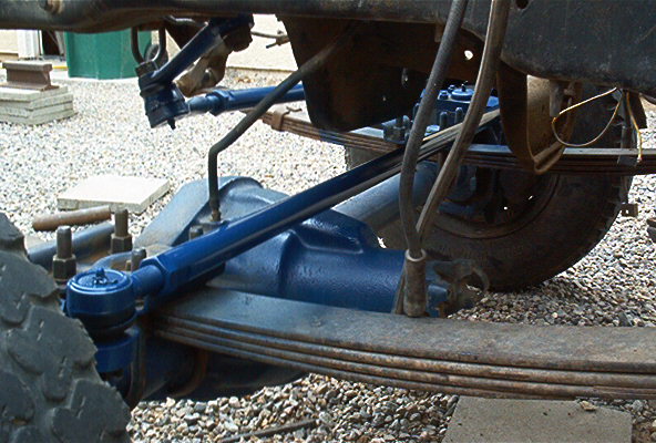 Close-up of blue-painted leaf-sprung solid front axle with tie rod and drag link