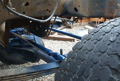 1986 Ford Bronco - The underside of a vehicle shows its suspension system and frame, with a large tire dominating the foreground.