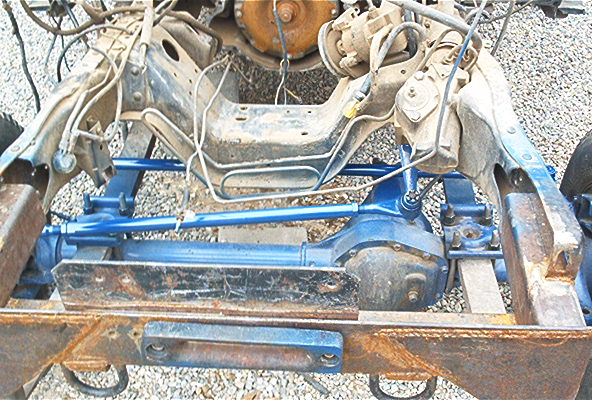 Bare truck frame with blue-painted Dana front axle, radius arms and tie rod installed