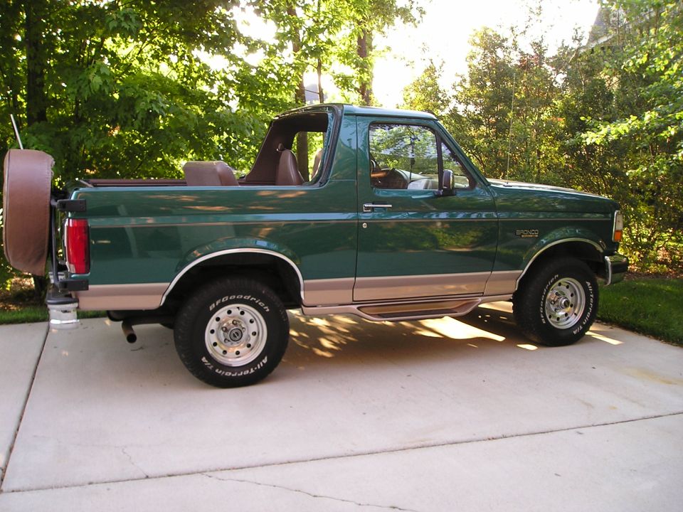 Green and tan Ford Bronco SUV, top removed, side view on driveway