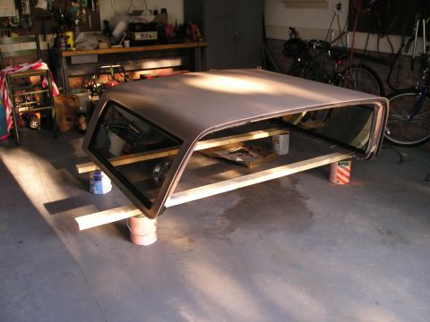 1996 Ford Bronco - A car roof section, possibly from a Bronco, is stored on wooden supports in a garage.