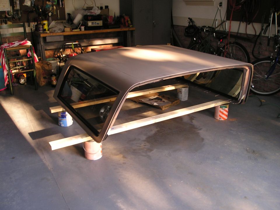 Tan Ford Bronco removable hardtop with tinted glass resting on planks and paint cans in a garage