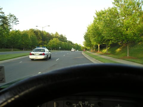 1996 Ford Bronco - A police car is seen from the perspective of another vehicle on a tree-lined road.