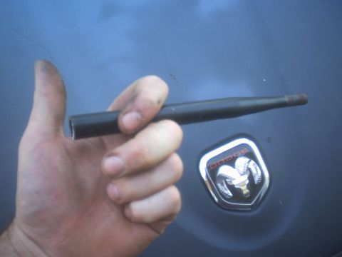 1991 Ford Crown Victoria - A hand holds a metal rod in front of a Dodge emblem, likely a part for a vehicle.
