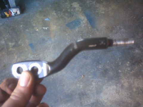 1991 Ford Crown Victoria - A metal lever part is held up against a concrete floor, with a Supermotors.net logo visible.