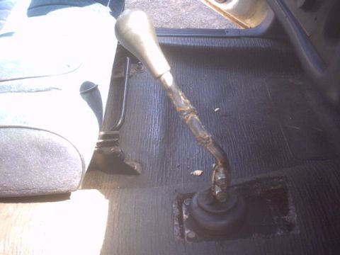 1991 Ford Crown Victoria - The interior of a vehicle shows a gear shifter with a taped handle and a black ribbed floor mat.