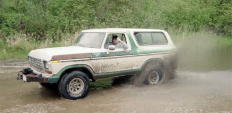 1978 Ford Bronco - A 1978 Ford Bronco navigates a muddy terrain, with water splashing around its tires.