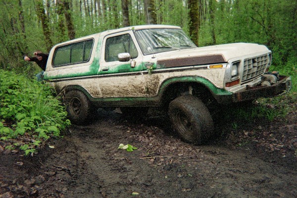 Green and white 1970s Ford Bronco articulating suspension on a muddy forest trail