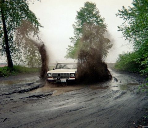 1978 Ford Bronco - A truck navigates a very muddy and waterlogged road, creating large splashes.