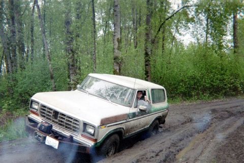 1978 Ford Bronco - A 1978 Ford Bronco navigates a muddy trail through a wooded area.