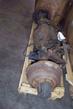 1996 Ford Bronco - A rusty used solid axle assembly strapped to a wooden shipping pallet on a concrete floor, with brake drums and hubs still attached at both…