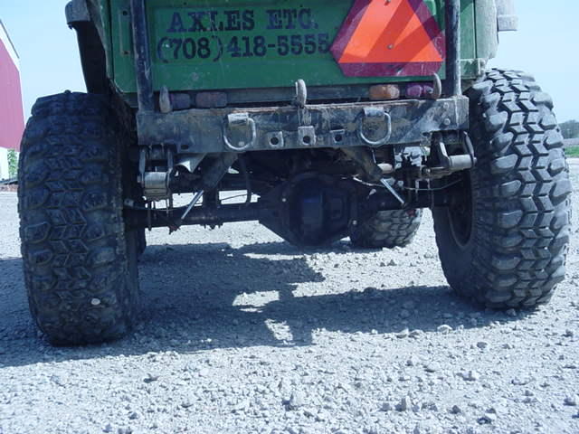 Rear view of a green off-road vehicle with large tires, showing the axle and suspension. Text on the back reads 'AXLES ETC. (708) 418-5555'