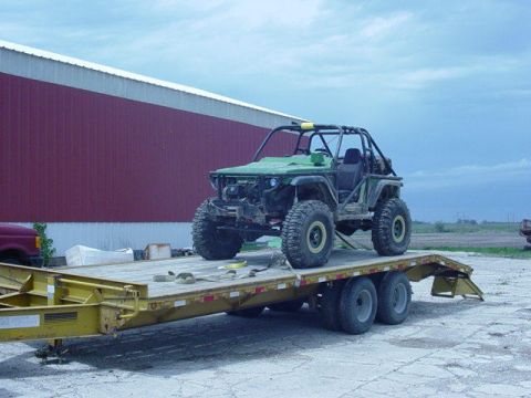 1992 Ford Bronco - A custom-built green off-road buggy is transported on a flatbed trailer, with a large red barn in the background.