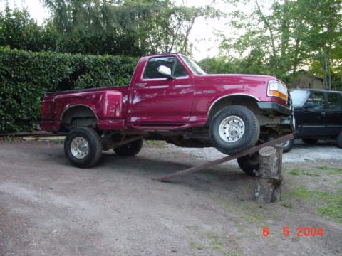 1992 Ford F-150 - A red 1992 Ford F-150 pickup truck is shown with its front wheels elevated on a ramp and log.