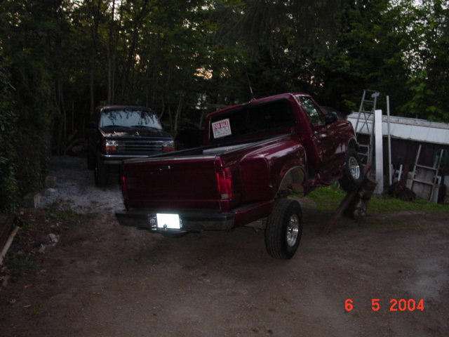Red pickup truck with a "For Sale" sign in the window, lifted on a stand, rear view