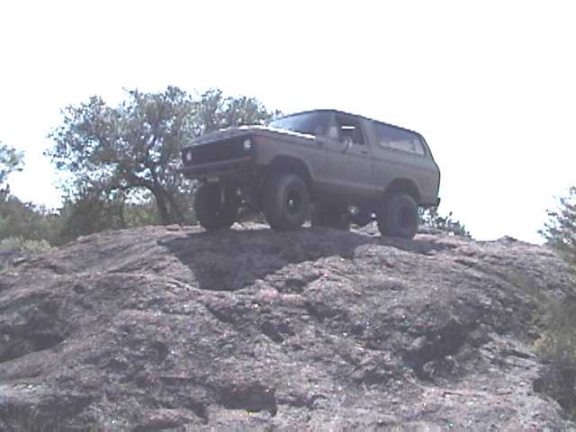 Lifted Ford Bronco hardtop perched on a granite dome against a bright sky