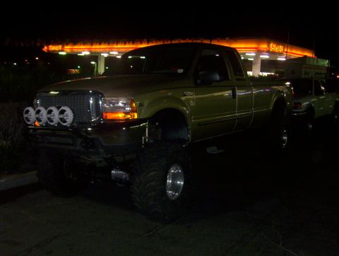 2000 Ford F-450 - A lifted gold Ford F-Series truck is parked at a gas station at night, with another vehicle visible behind it.