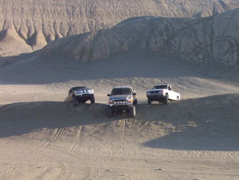 2000 Ford F-450 - Several trucks navigate a sandy terrain with large hills in the background.