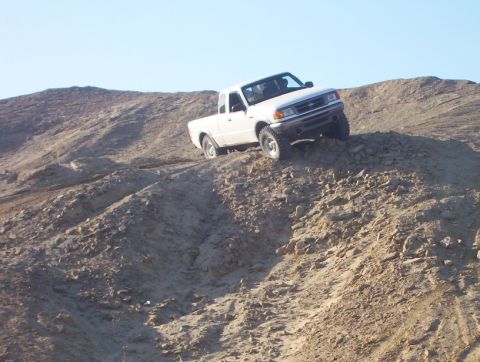 2000 Ford F-450 - White pickup truck navigating a steep dirt incline under a clear blue sky.