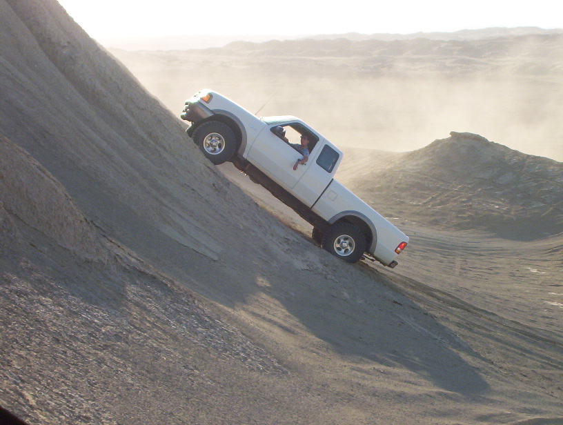 White pickup truck driving up a steep dirt hill. Driver is visible
