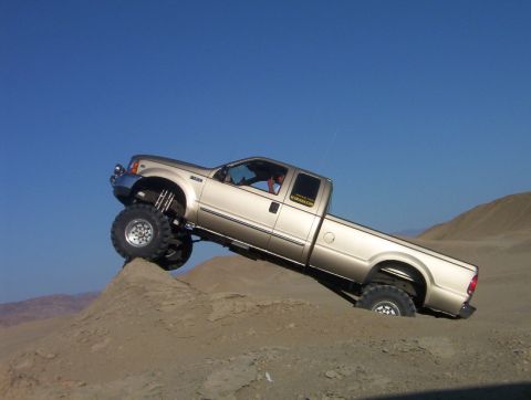 2000 Ford F-450 - A gold 2000 Ford F-450 pickup truck navigates a steep sand dune under a clear blue sky.