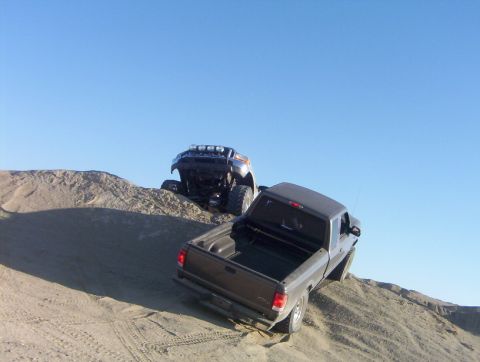 2000 Ford F-450 - Two trucks navigate sandy terrain on a clear day.