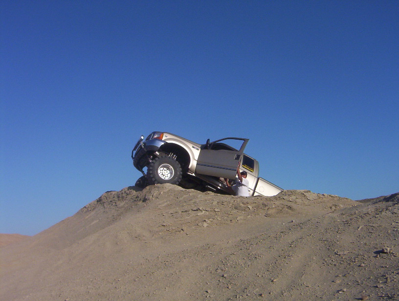 Silver 2000 Ford F-450 on its side on a sand dune, driver's door open