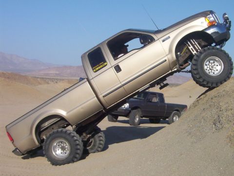 2000 Ford F-450 - A lifted pickup truck navigates a sandy hill, with another truck visible in the background.