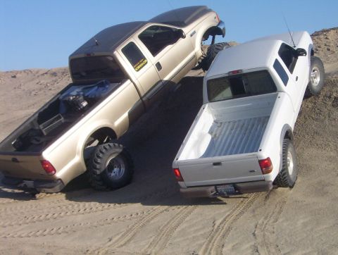 2000 Ford F-450 - Two pickup trucks, a gold Ford F-450 and a white truck, navigate a sandy hill with modified suspensions.