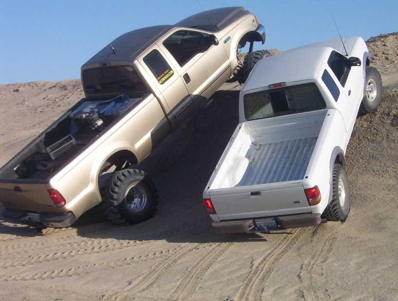 Gold 2000 Ford F-450 and white pickup truck climbing a sand dune, both with lifted suspensions