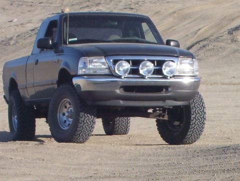 2000 Ford F-450 - A black pickup truck with off-road tires and auxiliary lights is parked on a dirt surface.