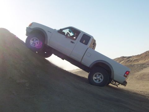 2000 Ford F-450 - A white pickup truck navigates a steep sand dune under a bright sky.