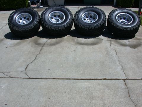 1996 Ford Bronco - Four large off-road tires and rims are displayed on a cracked concrete surface.