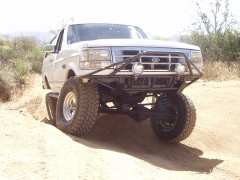 1993 Ford Bronco - A modified white Ford Bronco navigates a dusty off-road trail.
