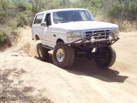 1993 Ford Bronco - This lifted 1993 Ford Bronco navigates a dusty trail, its off-road capabilities with a custom bumper and aggressive tires.