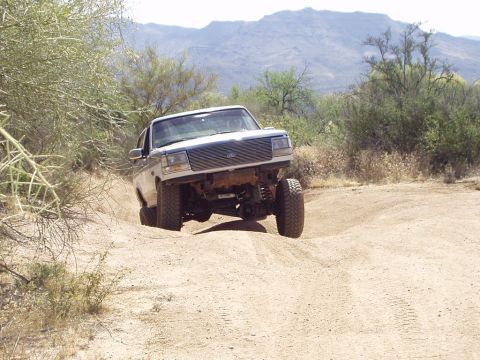 1993 Ford Bronco - A Ford Bronco navigates a dusty off-road trail in a mountainous desert landscape.