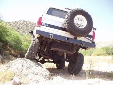 1993 Ford Bronco - Ford Bronco navigating an off-road obstacle, showing its rear suspension and spare tire.
