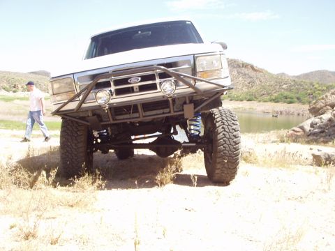 1993 Ford Bronco - A modified Ford truck is shown off-road near a lake with a person walking in the background.
