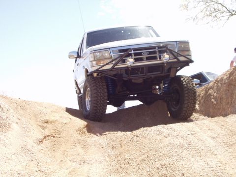1993 Ford Bronco - A lifted Ford Bronco navigates a dirt hill with another vehicle visible in the background.
