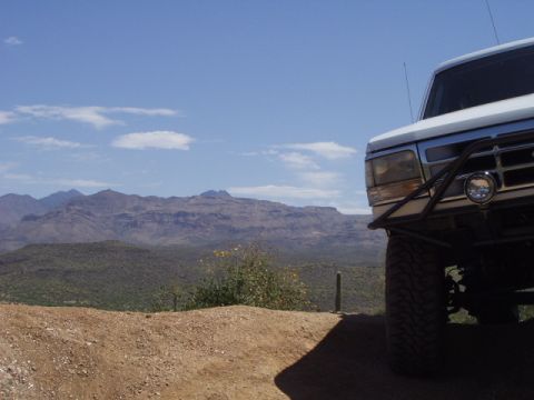 1993 Ford Bronco - A white Ford Bronco is parked on a dirt road with a desert mountain range in the background.