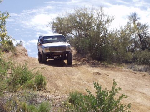 1993 Ford Bronco - A white 1993 Ford Bronco navigates a dusty, off-road trail with sparse desert vegetation.