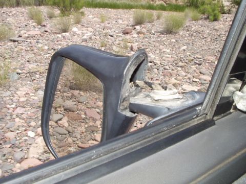 1993 Ford Bronco - The side mirror is detached and hanging loose, revealing internal damage and the rocky terrain beyond.