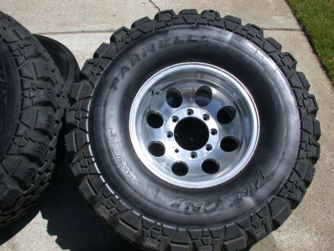 1996 Ford Bronco - A set of aggressive off-road tires and polished aluminum wheels are shown resting on a concrete surface.