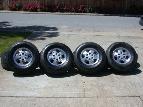 1996 Ford Bronco - Four tires and rims are lined up on a concrete surface in front of a wooden fence.