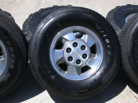 1996 Ford Bronco - Four tires and rims are displayed on a concrete surface. One of the rims features a Chevrolet emblem.